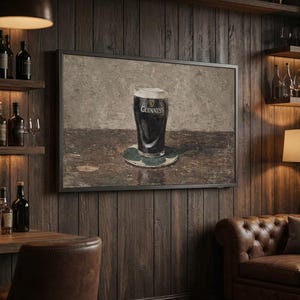 May include: A framed print of a pint of Guinness stout on a coaster. The artwork depicts the dark beer with a creamy head, set against a neutral background. The Guinness logo is visible on the glass. The print is displayed in a pub setting.