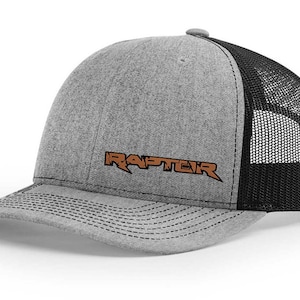 May include: A gray and black trucker hat with a brown embroidered logo that says "RAPTOR".