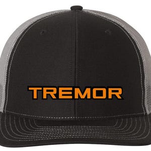 May include: Black and gray trucker hat with the word "TREMOR" in orange block letters across the front. The hat has a curved brim and a mesh back for ventilation. The hat is a classic style.