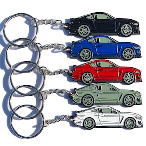 May include: Five keychains featuring a detailed die-cast model of a Ford Mustang. The keychains are available in black, blue, red, green, and white.