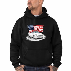 May include: Black hooded sweatshirt featuring a white car graphic with an American flag waving in the background. The car is a convertible. The design is a patriotic theme.
