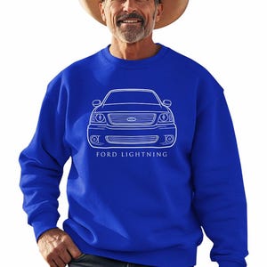 May include: Royal blue sweatshirt featuring a white outline of a Ford Lightning truck. The text "FORD LIGHTNING" is printed below the vehicle illustration. The person in the image is wearing a cowboy hat.
