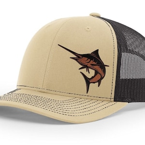 May include: A beige and black trucker hat with a brown marlin fish embroidered on the front.