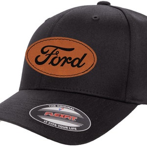 May include: Black baseball cap with a brown leather oval patch that says "Ford" in a cursive font. The cap has a Flexfit label on the underside of the brim.