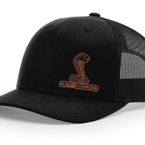 May include: Black and brown trucker hat with a brown embroidered cobra and the text "GT 500".