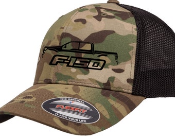 May include: A camouflage and black trucker hat with a black silhouette of a Ford F-150 pickup truck and the text "F-150" in gold lettering. The hat has a Flexfit label on the back.