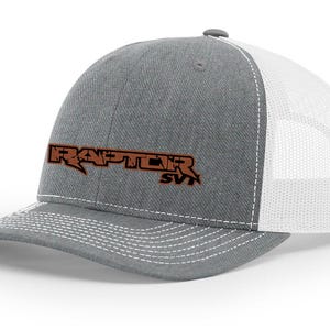 May include: A gray and white trucker hat with a brown embroidered logo that says "RAPTOR SVT".