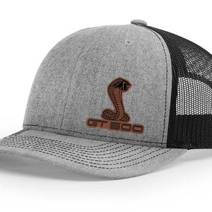 May include: A gray and black trucker hat with a brown leather patch featuring a cobra and the text "GT 500".