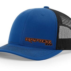 May include: A blue and black trucker hat with a brown embroidered logo that says "RAPTOR SVT".