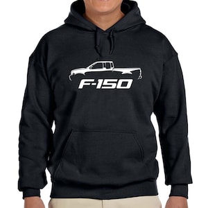 Può includere: Una felpa con cappuccio nera con un contorno bianco di un pick-up Ford F-150 e il testo "F-150" stampato sul davanti.
