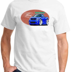 May include: A white t-shirt with a blue Ford Lightning pickup truck cartoon illustration. The truck is on a brick background with the words "The Lightning Ford Motor Co." and "Lightning Alley" on a green street sign.