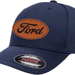 May include: A navy blue baseball cap with a brown leather patch featuring the Ford logo. The cap has a Flexfit label on the underside of the brim.