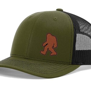 May include: A green and black trucker hat with a brown silhouette of Bigfoot walking on the front.