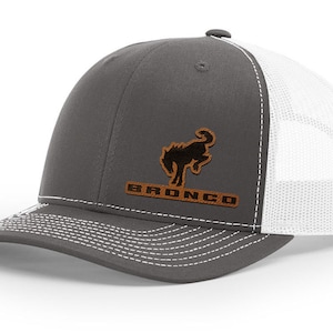 May include: A gray and white trucker hat with a brown leather patch featuring a black silhouette of a rearing horse and the word "BRONCO" in brown lettering.