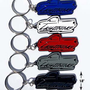 May include: Five Ford Lightning truck keychains in different colors: blue, white, red, gray, and black. Each keychain is 2.5 inches wide and 1 inch tall. The keychains are made of metal and have a black outline.