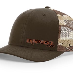 May include: A brown and tan camouflage trucker hat with a brown front panel and a brown "RAPTOR SVT" logo embroidered on the front.