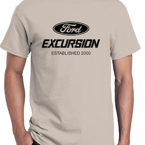 Puede incluir: Una camiseta beige claro con un logotipo negro de Ford Excursion y el texto "Establecido en 2000".