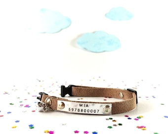 May include: A brown suede cat collar with a silver name tag that reads "MIA 6978800007". The collar has a small silver bell attached.