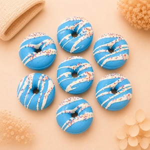 Könnte beinhalten: Sieben runde, donut-förmige Objekte mit leuchtend blauer Glasur, weißen Glasurstreifen und bunten Streuseln, die in einem Kreis angeordnet sind. Jeder Artikel hat ein Loch in der Mitte und eine glatte, glänzende Oberfläche in Blau.