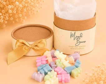 Könnte beinhalten: Eine zylindrische Pappschachtel mit einer goldenen Schleife, gefüllt mit weißem Seidenpapier und kleinen, bunten, bärenförmigen Wachsschmelzen. Die Schachtel ist mit Mixed Bears, Mixed Fruit Scented Bear Wax Melts und CNT beschriftet.