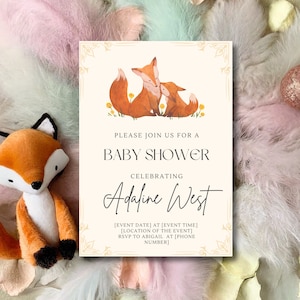 May include: A baby shower invitation featuring watercolor foxes and the text "Please join us for a baby shower celebrating Adaline West." A plush fox toy is next to the invitation. The invitation is on a cream background.