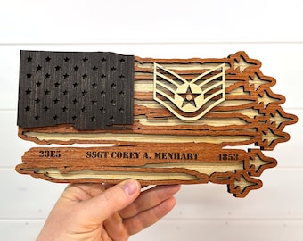 May include: A wooden American flag with a distressed look, featuring a  US Air Force E-5 Sergeant rank insignia, the name "SSGT COREY A. MENHART", and the numbers "23E5" and "4853".