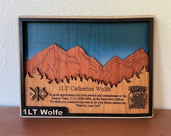 Puede incluir: Una placa de madera con una escena de montaña y un cielo azul. La placa tiene el texto "1LT Catherine Wolfe" y "En gran aprecio por su servicio y compromiso con el equipo Reaper, C Co 299th BHB, como oficial ejecutivo. Le deseamos mucho éxito en todos sus futuros esfuerzos. "Primero en entrar, último en salir!" 1LT Wolfe" y un logotipo que dice "REAPERS".