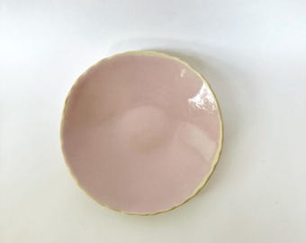 May include: A small, pink ceramic dish with a scalloped edge and a light yellow rim.