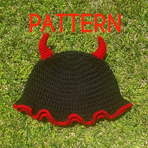 以下が含まれることがあります： 赤い悪魔の角が付いた黒いクロシェのバケットハット。ハットはフリルのある縁をしています。