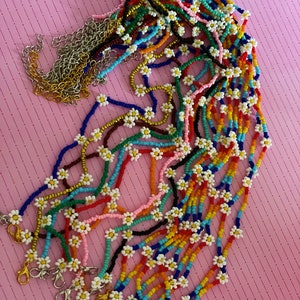 May include: A collection of colorful beaded necklaces with daisy-shaped charms. Each necklace has a silver clasp.