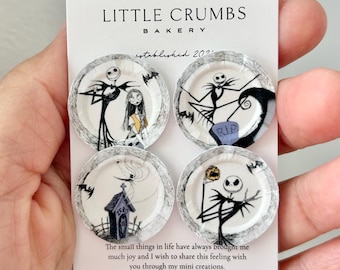 May include: Four miniature round plates featuring black and white illustrations of characters from The Nightmare Before Christmas, displayed on a white card labeled Little Crumbs Bakery with text about sharing joy through mini creations.