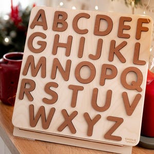 Op de afbeelding: Houten alfabetpuzzel met hoofdletters A tot en met Z in bruin op een lichte houten achtergrond.