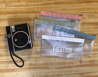 May include: Four clear plastic zippered pouches with different colored trim. The pouches are stacked on top of each other. The top pouch has pink trim, the second pouch has green trim, the third pouch has blue trim, and the bottom pouch has white trim. The bottom pouch has the word "Vacation" printed on it in white.