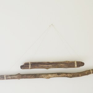May include: Two pieces of driftwood are hung on a white wall with twine. The driftwood is brown and has a natural, rustic look.