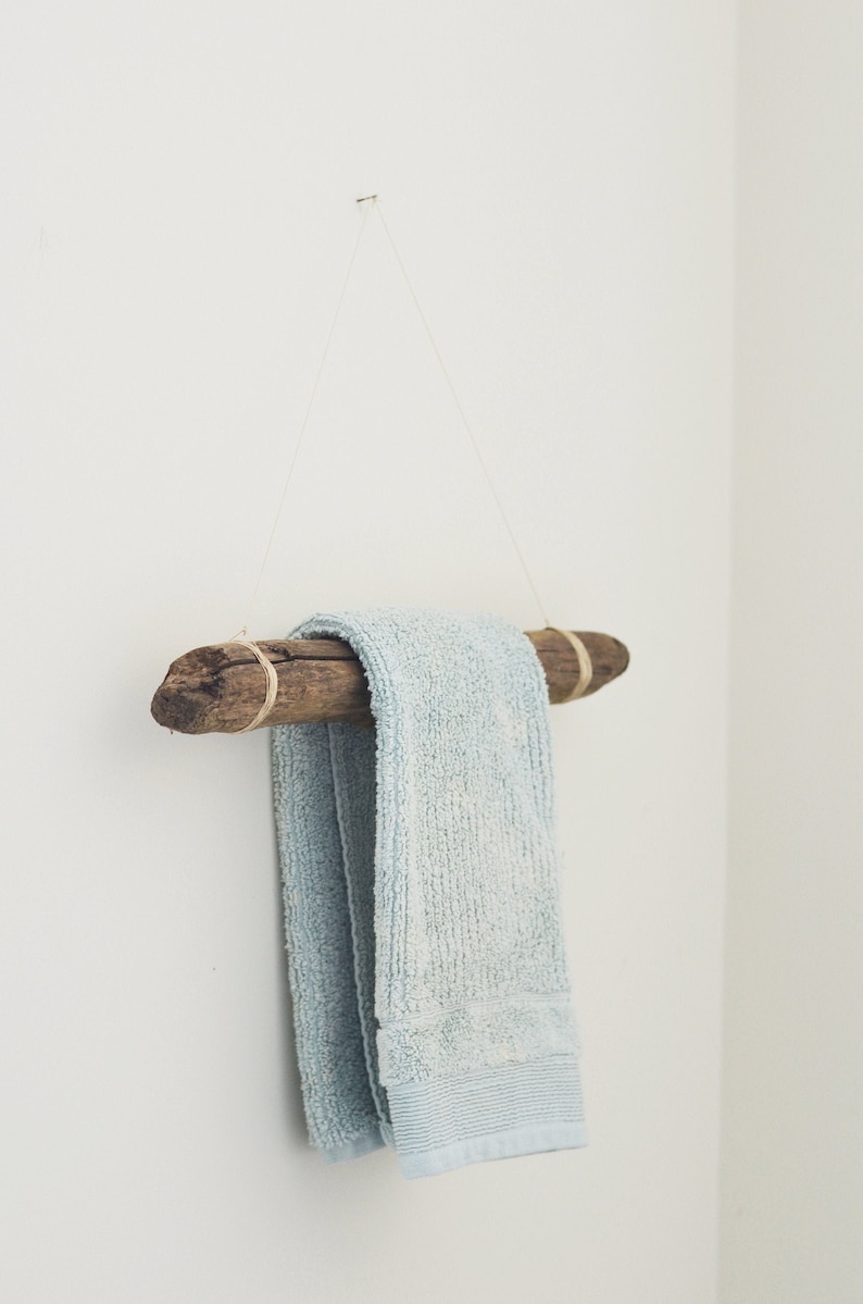 May include: A light blue towel hanging on a rustic wooden towel rack made from driftwood. The rack is suspended from the ceiling with twine.