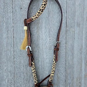 May include: A brown leather horse headstall with a braided rope headstall featuring a black and tan pattern. The headstall has a leather browband and a leather noseband.