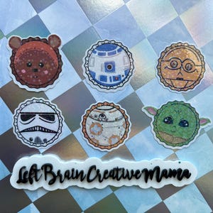 May include: Six round, white, glitter-covered stickers with various Star Wars characters. The characters include Yoda, R2-D2, a Stormtrooper, a brown bear, and two other characters. The stickers are arranged in two rows of three. The text "Left Brain Creative Mama" is printed on a white sticker below the characters.