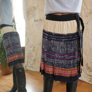 May include: A pleated skirt with a cream colored top section and a blue and white patterned bottom section. The skirt has a black waistband and a black tie.