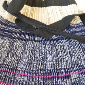 May include: A pleated skirt with a blue and white patterned design. The skirt has a black ribbon tied around the waist and a pink stripe at the bottom.