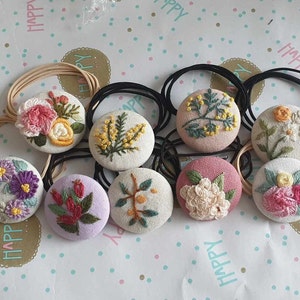 May include: A set of 10 handmade hair ties with embroidered floral designs. Each tie features a different floral pattern, including roses, daisies, and sprigs of leaves. The ties are made with a soft, white fabric and are perfect for adding a touch of elegance to any hairstyle.