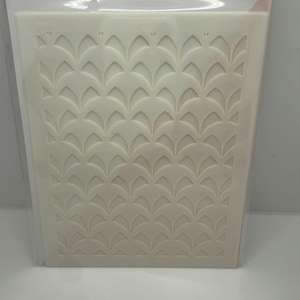 May include: A white Geo Arch stencil with a repeating geometric pattern. The stencil is packaged in a clear plastic sleeve. The packaging includes the text "pinkfresh studio" and "Crafting stencil".