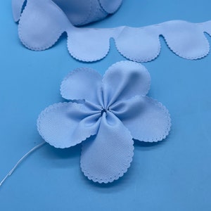 May include: A light blue fabric flower with scalloped edges. The flower is made from a ribbon and is tied together in the center.