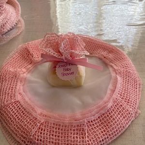 Könnte beinhalten: Eine rosa und weiße Häkeldeckchen mit einer kleinen rosa und weißen Geschenkverpackung in der Mitte. Die Geschenkverpackung hat einen Anhänger mit der Aufschrift "Josephine Baby Shower".