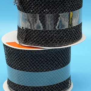 Puede incluir: Dos carretes de cinta de malla negra con purpurina. La cinta está envuelta alrededor de carretes de cartón blanco con etiquetas naranjas.