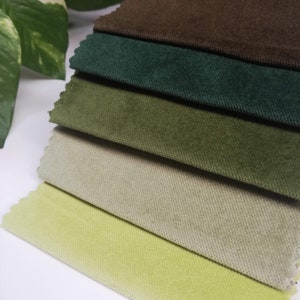 May include: A stack of six fabric swatches in various shades of green, brown, and beige. The swatches are arranged from darkest to lightest, with the brown swatch on top and the lightest beige swatch on the bottom.