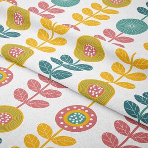 May include: White fabric with a repeating floral pattern. The design features stylized flowers and leaves in yellow, teal, pink, and green. The fabric is folded, showing the pattern's repeat.