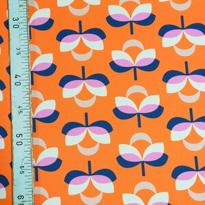 K&ouml;nnte beinhalten: Orangener Stoff mit einem sich wiederholenden Blumenmuster. Das Design zeigt stilisierte Blumen in Wei&szlig;, Rosa und Marineblau. Ein Lineal ist am linken Rand sichtbar, das die Ma&szlig;e in Zentimetern anzeigt.
