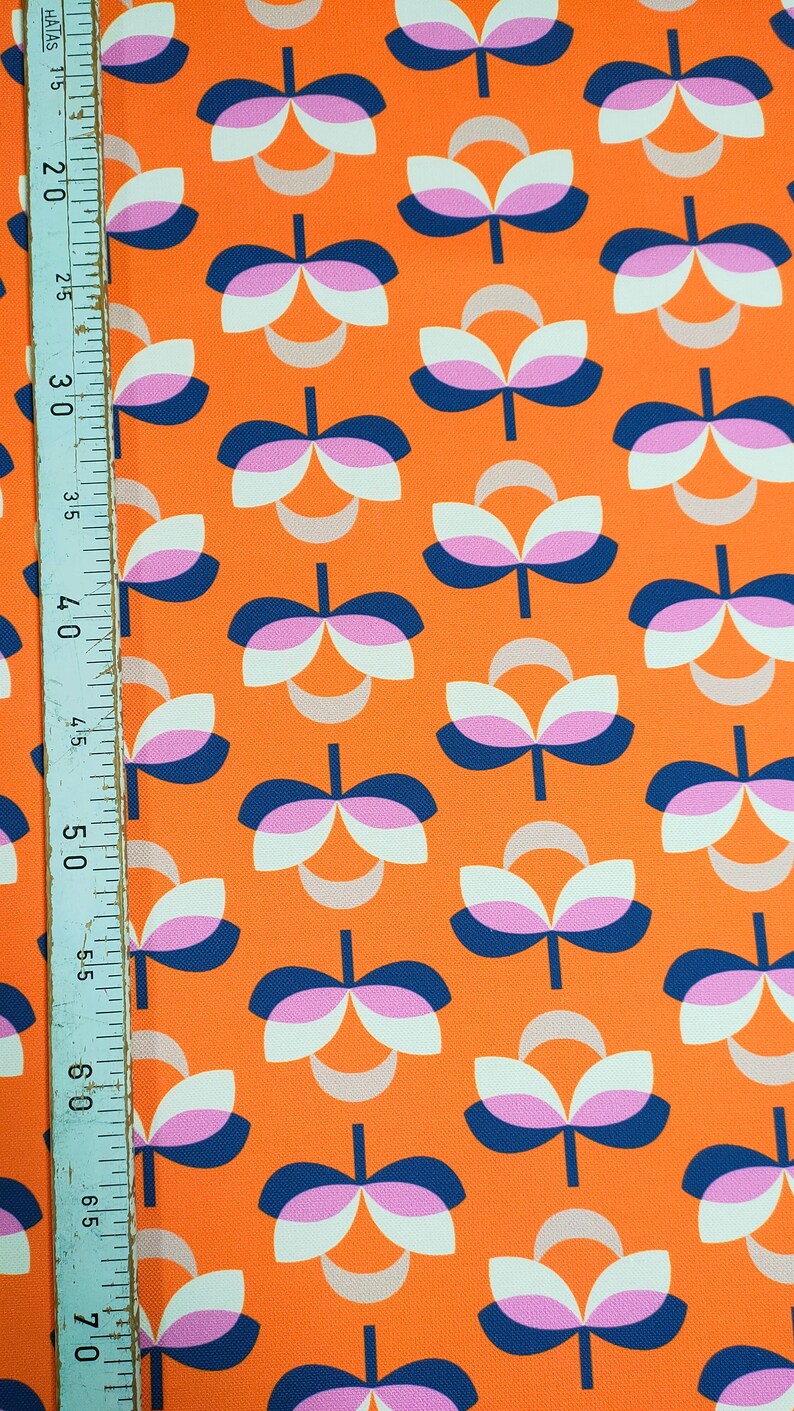 K&ouml;nnte beinhalten: Orangener Stoff mit einem sich wiederholenden Blumenmuster. Das Design zeigt stilisierte Blumen in Wei&szlig;, Rosa und Marineblau. Ein Lineal ist am linken Rand sichtbar, das die Ma&szlig;e in Zentimetern anzeigt.