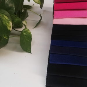 May include: A stack of fabric swatches in various colors, including pink, red, blue, and black. The swatches are arranged in a vertical stack, with the pink swatches at the top and the black swatches at the bottom.