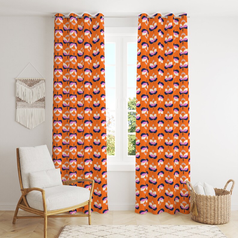 K&ouml;nnte beinhalten: Orangefarbene Vorh&auml;nge mit Blumenmuster. Die Vorh&auml;nge zeigen ein sich wiederholendes Muster stilisierter Blumen in Wei&szlig;, Lila, Marineblau und Grau. Die Vorh&auml;nge h&auml;ngen vor einem Fenster, mit einem wei&szlig;en Stuhl und einem Weidenkorb im Raum.